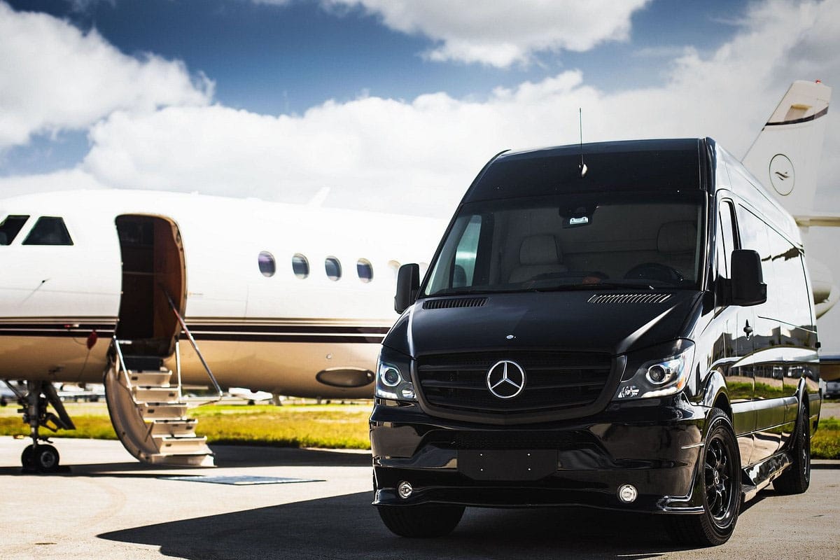 Black 2025 luxury van picking up passenger at Chicago O'Hare Airport terminal.